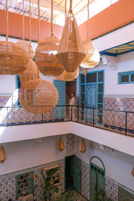 A woman is standing on a balcony in a building with wicker lamps hanging from the ceiling.