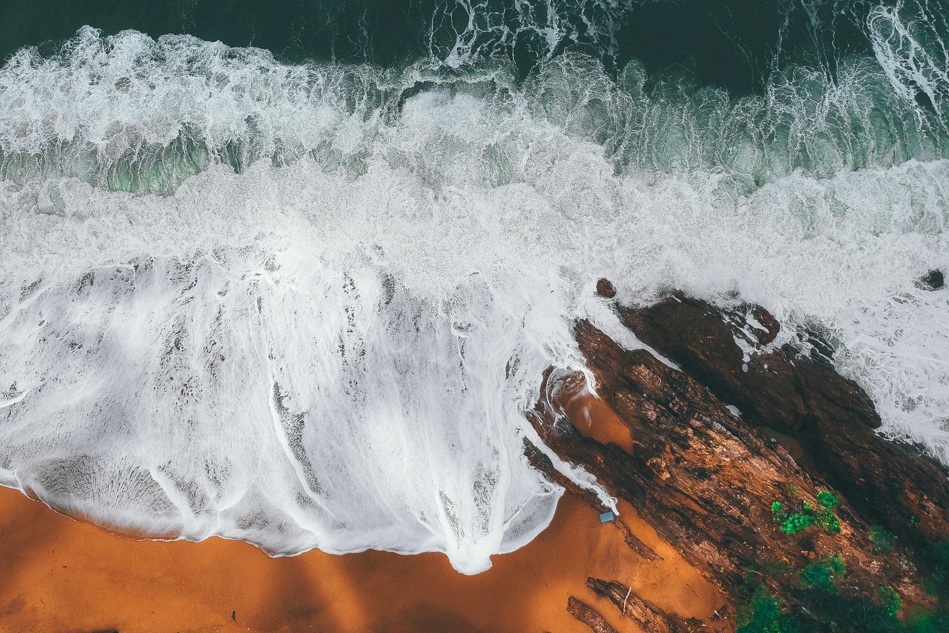 Aerial view of ocean waves crashing onto a rocky shore with white foam and turquoise water