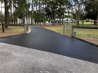 Freshly paved black driveway curving through a wooded park area with a gravel foreground