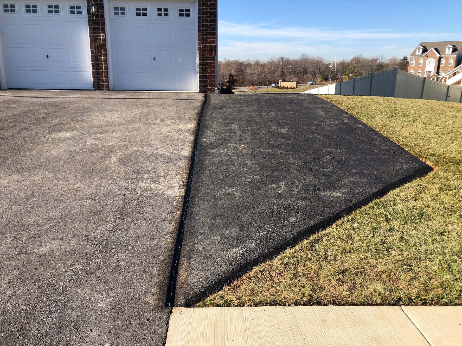 Concrete driveway with a dark asphalt patch beside a garage and grassy yard.