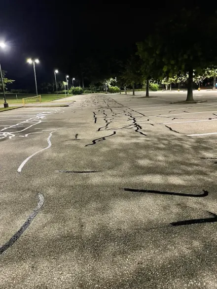 Cracked empty parking lot at night under streetlights with trees along the edge