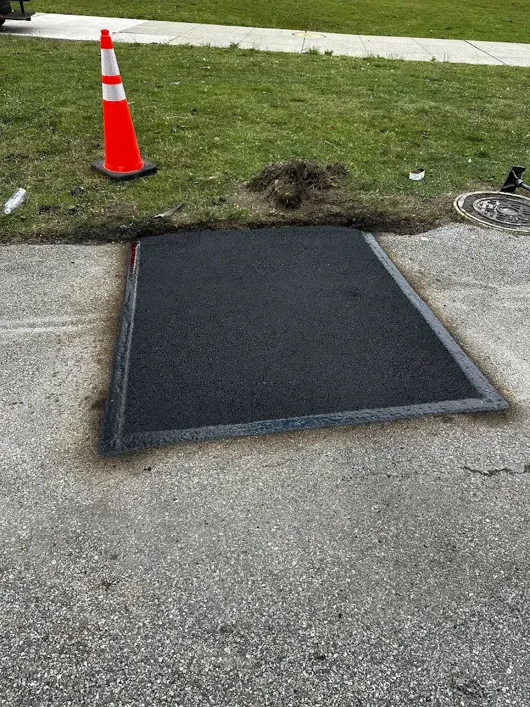 Black rubber wheelchair ramp mat on sidewalk beside grass and an orange traffic cone.