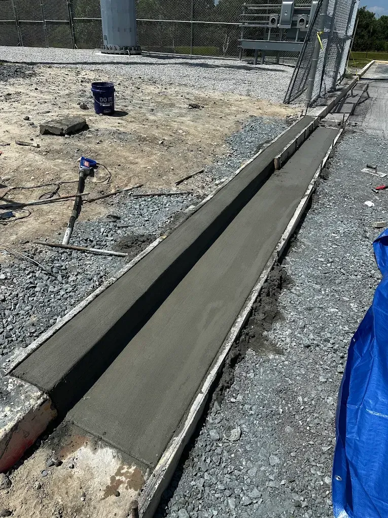 Fresh concrete curb or trench edge along a gravel construction site beside a roadway