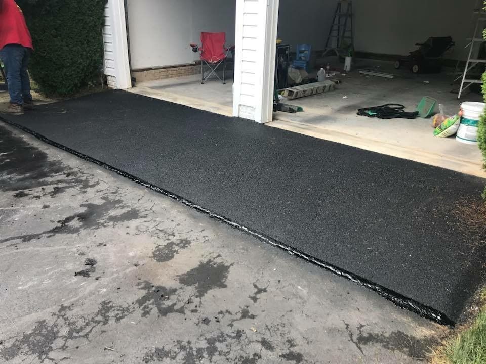 Freshly paved black asphalt ramp leading from a garage to a driveway, with tools visible inside the garage