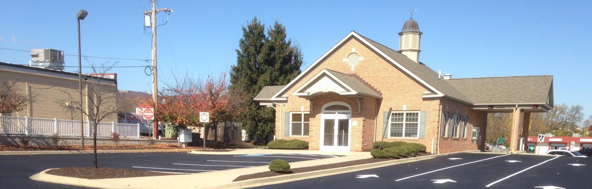 Small tan building with white trim beside a parking lot under a clear blue sky.