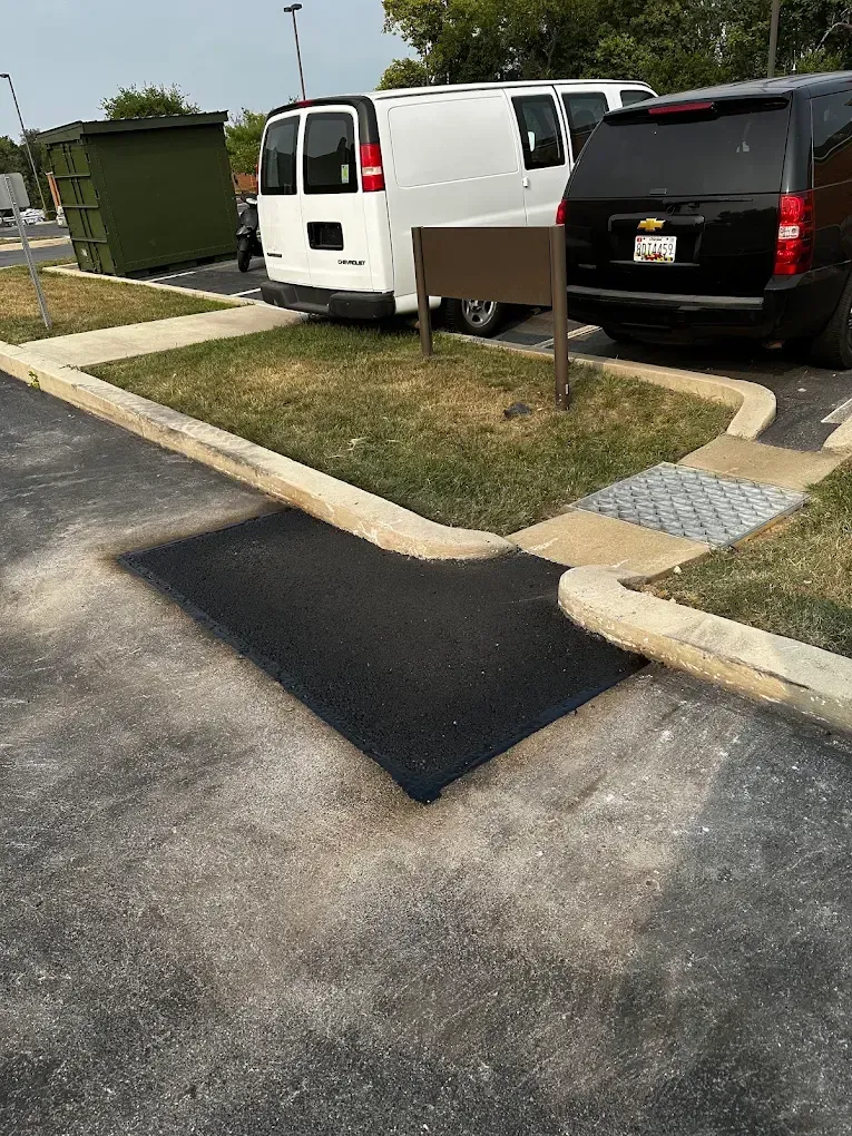 Parking lot curb ramp with a black van and white van beside a sidewalk and grassy strip