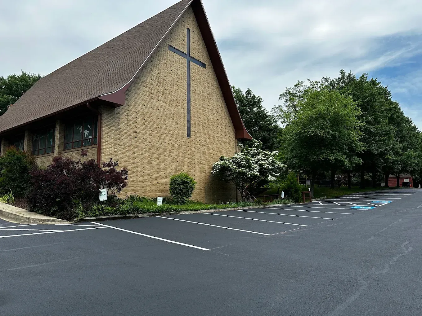 Stone church with a large cross on the front, beside an empty parking lot and trees