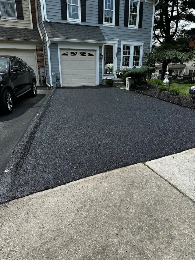 Fresh black asphalt driveway leading to a gray townhouse garage, with a car parked on the left.