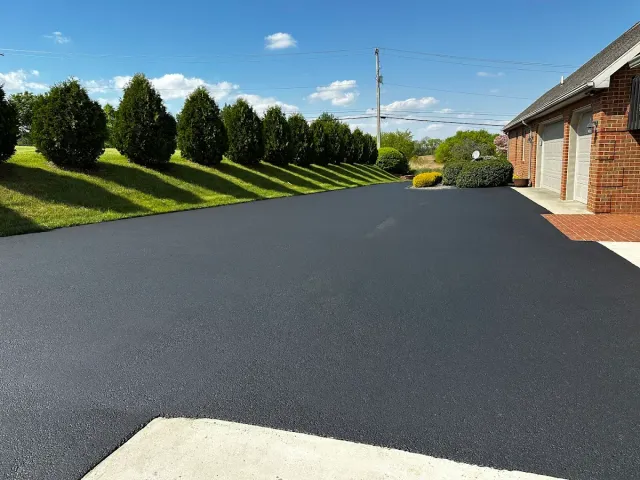 Empty paved driveway beside a brick house, with trimmed hedges and blue sky