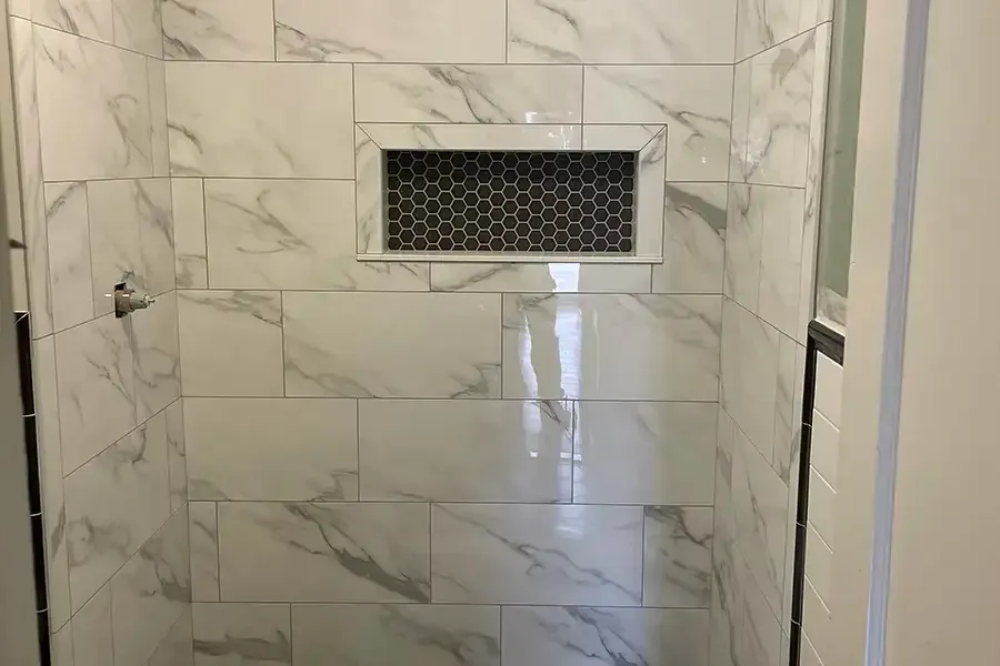 Tiled shower wall with a built-in niche and chrome shower controls on the left