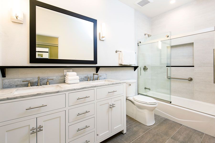 Bright modern bathroom with white vanity, large mirror, toilet, and glass shower enclosure