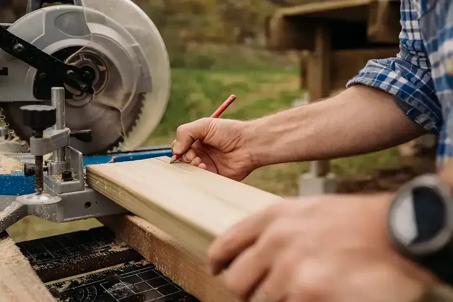 Person measuring a wooden plank on a miter saw in a workshop