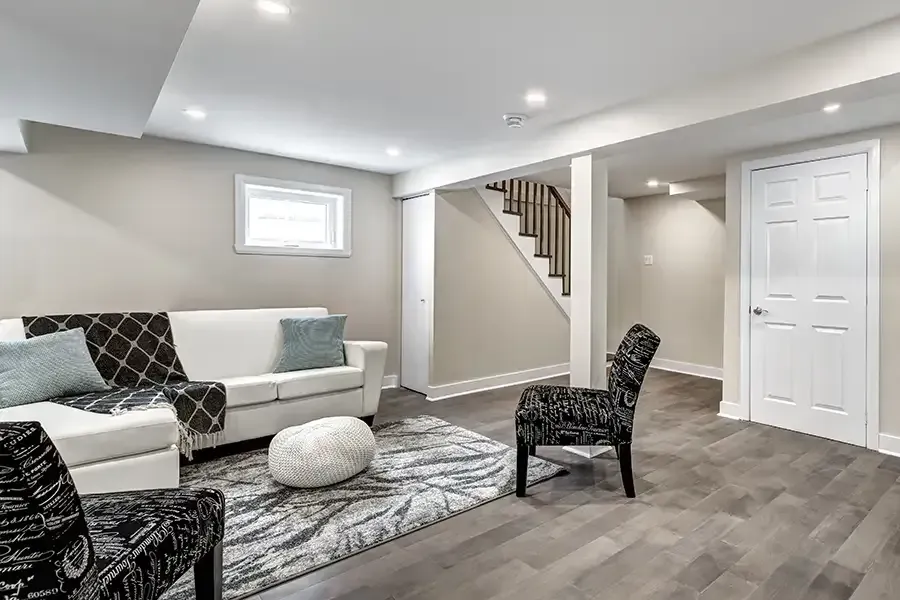 Bright modern living room with gray sofa, patterned chair, rug, staircase, and white doors