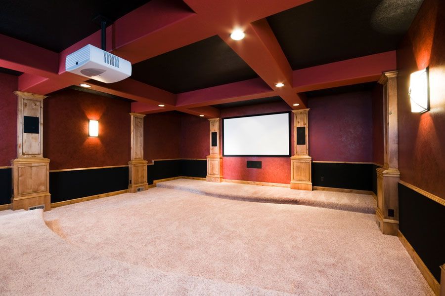 Empty home theater room with a large screen, wall sconces, and red and black decor.