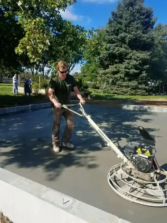 Worker smoothing wet concrete with a power trowel on a sunny outdoor construction site