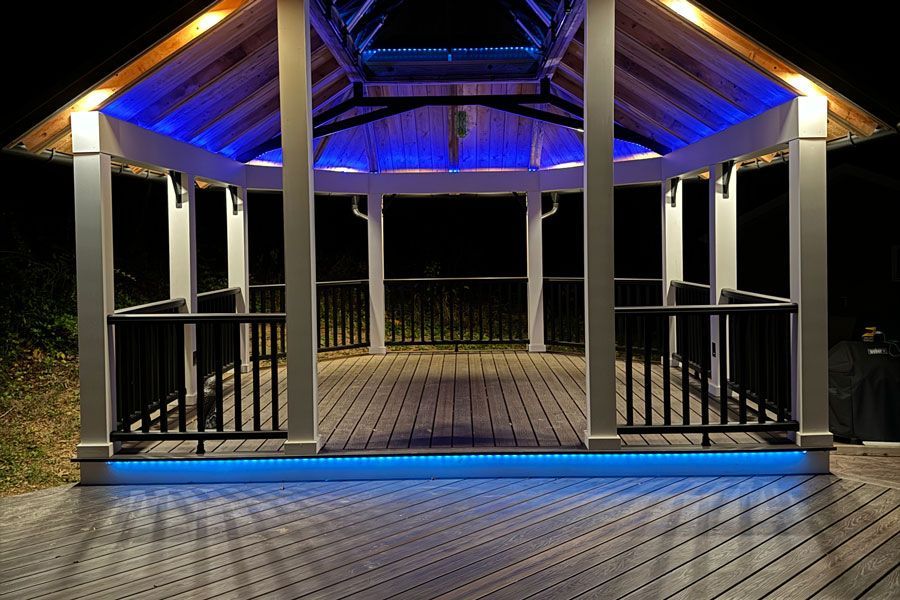 Illuminated wooden gazebo at night with blue accent lighting and railings on a boardwalk