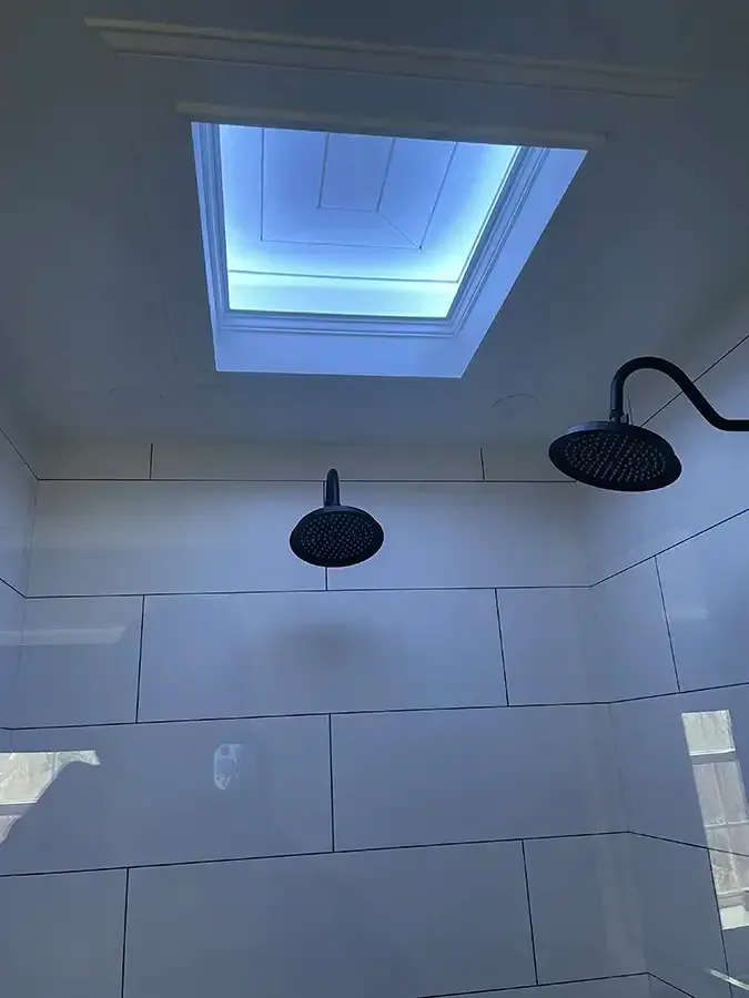 Modern bathroom shower with white tiled walls, black showerheads, and a skylight overhead