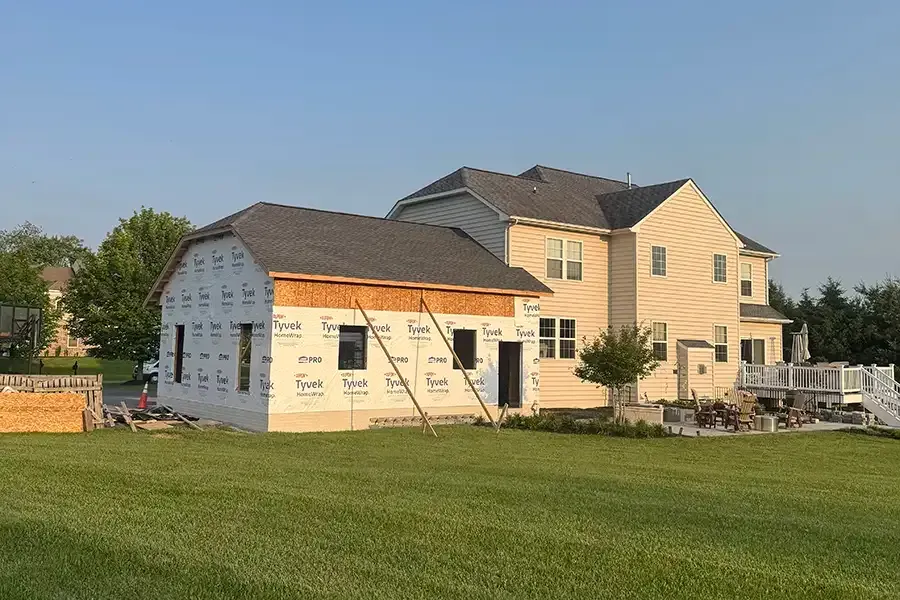 New addition under construction beside a finished beige home on a grassy lot at sunset