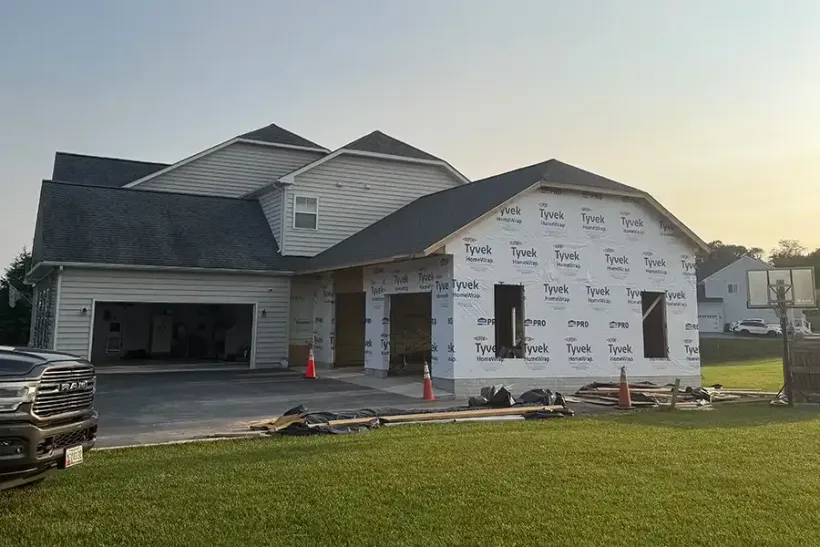 New house under construction with white wrap, gray roof, and an open garage at sunset