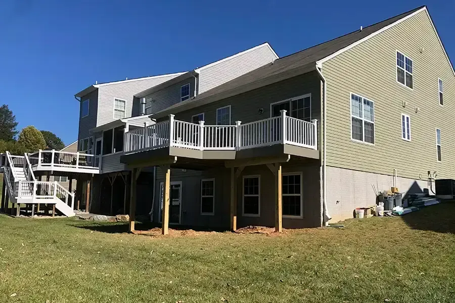 Suburban house exterior with beige siding, white balconies, and a grassy yard under a blue sky