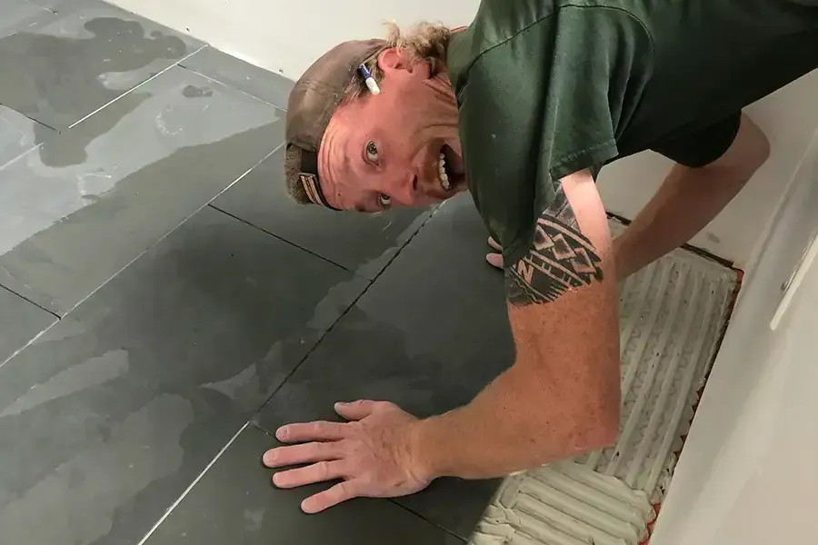 Man tiling a floor, crouched and reaching across wet gray tiles
