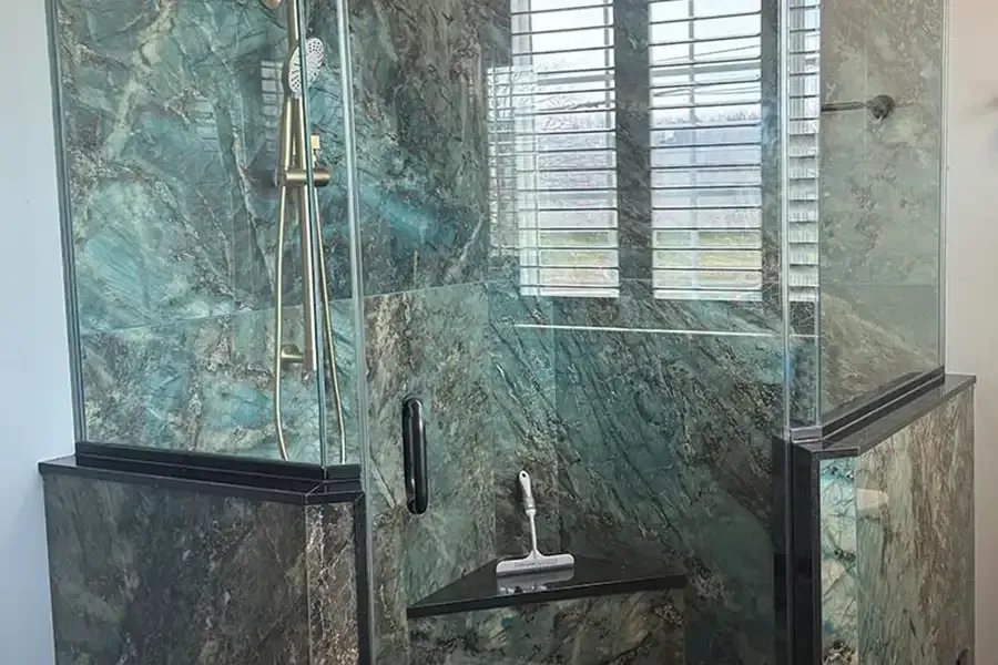 Glass shower enclosure with green marble tile walls and a built-in bench