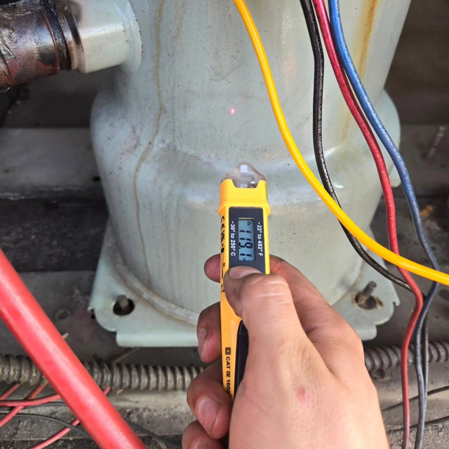 Hand holding a yellow electrical tester near wires on a metal machine base.