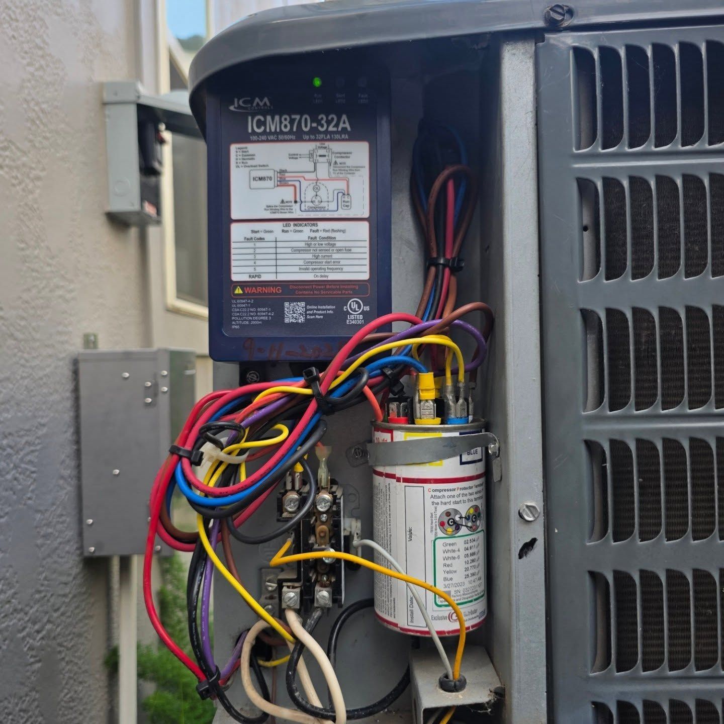 Open HVAC control panel with exposed wiring and a cylindrical capacitor.