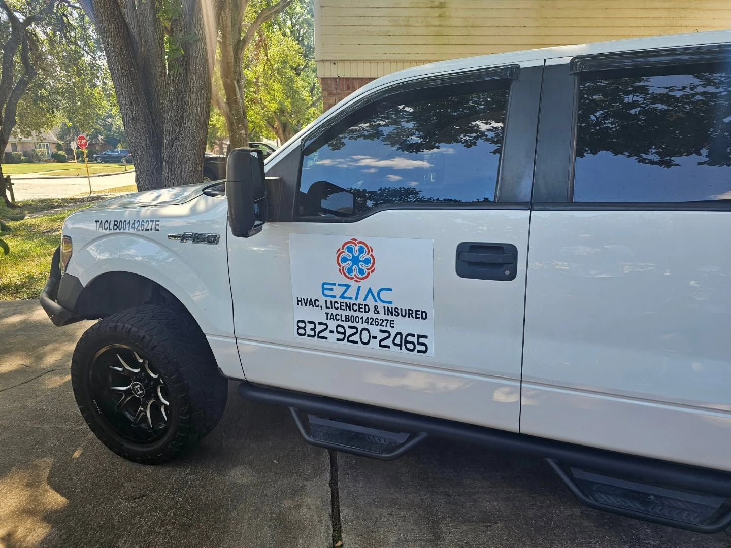 White EZJAC plumbing service truck parked by trees, with company logo and phone number on the door
