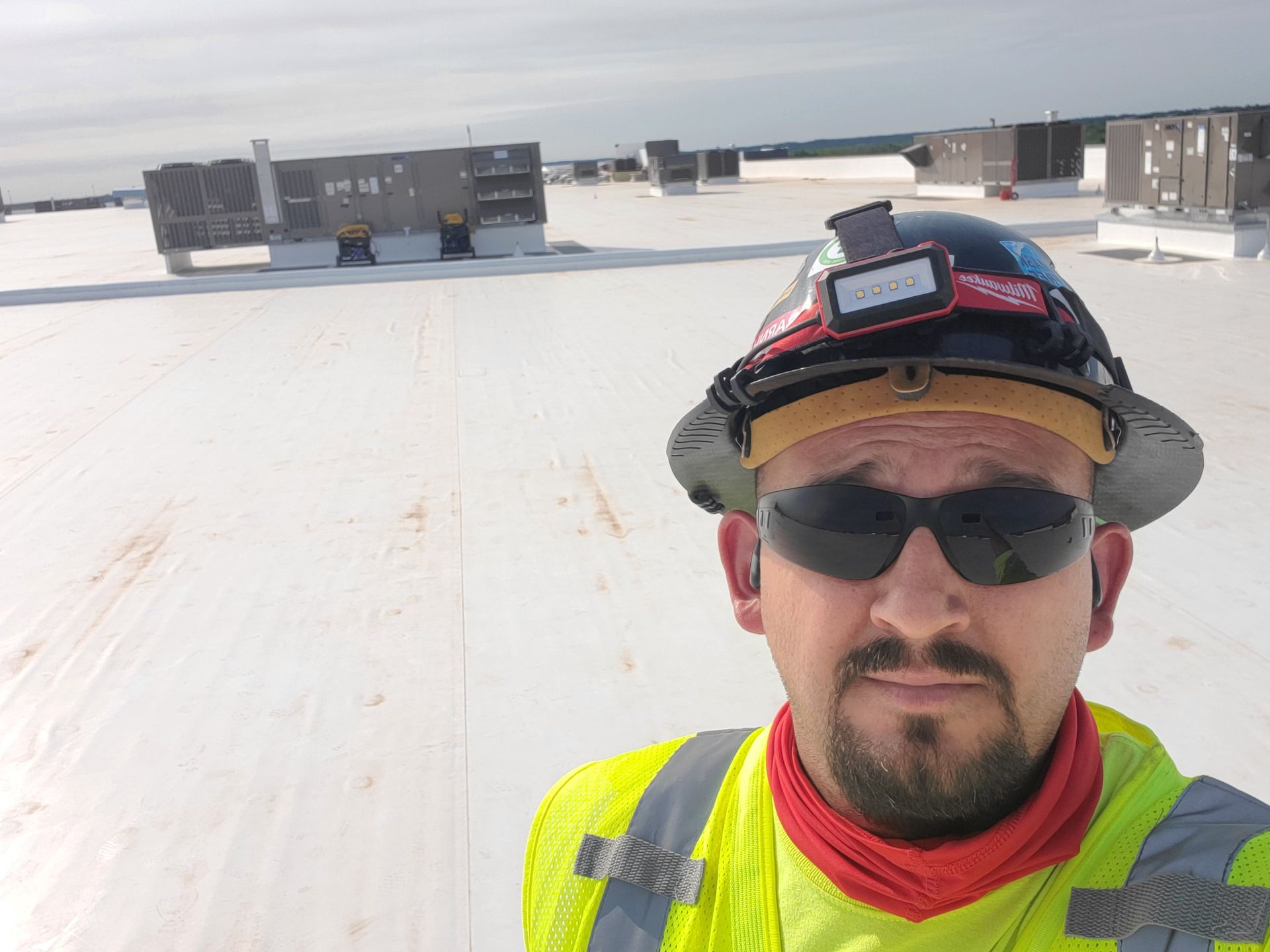 Man in safety gear on a white rooftop, wearing sunglasses and a hard hat with a headlamp.