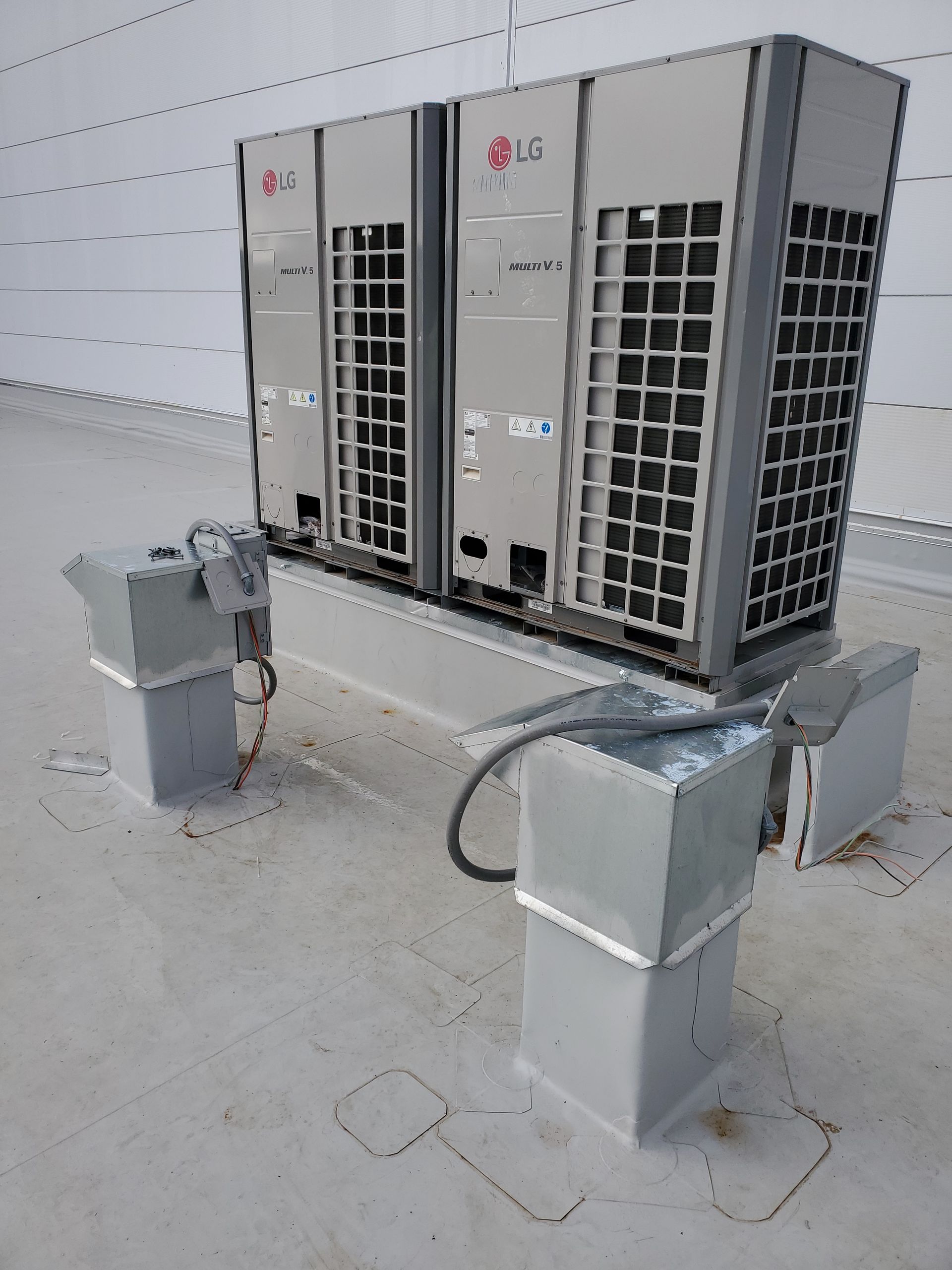 Two LG HVAC units on a raised platform atop a white rooftop. Gray electrical conduit visible.