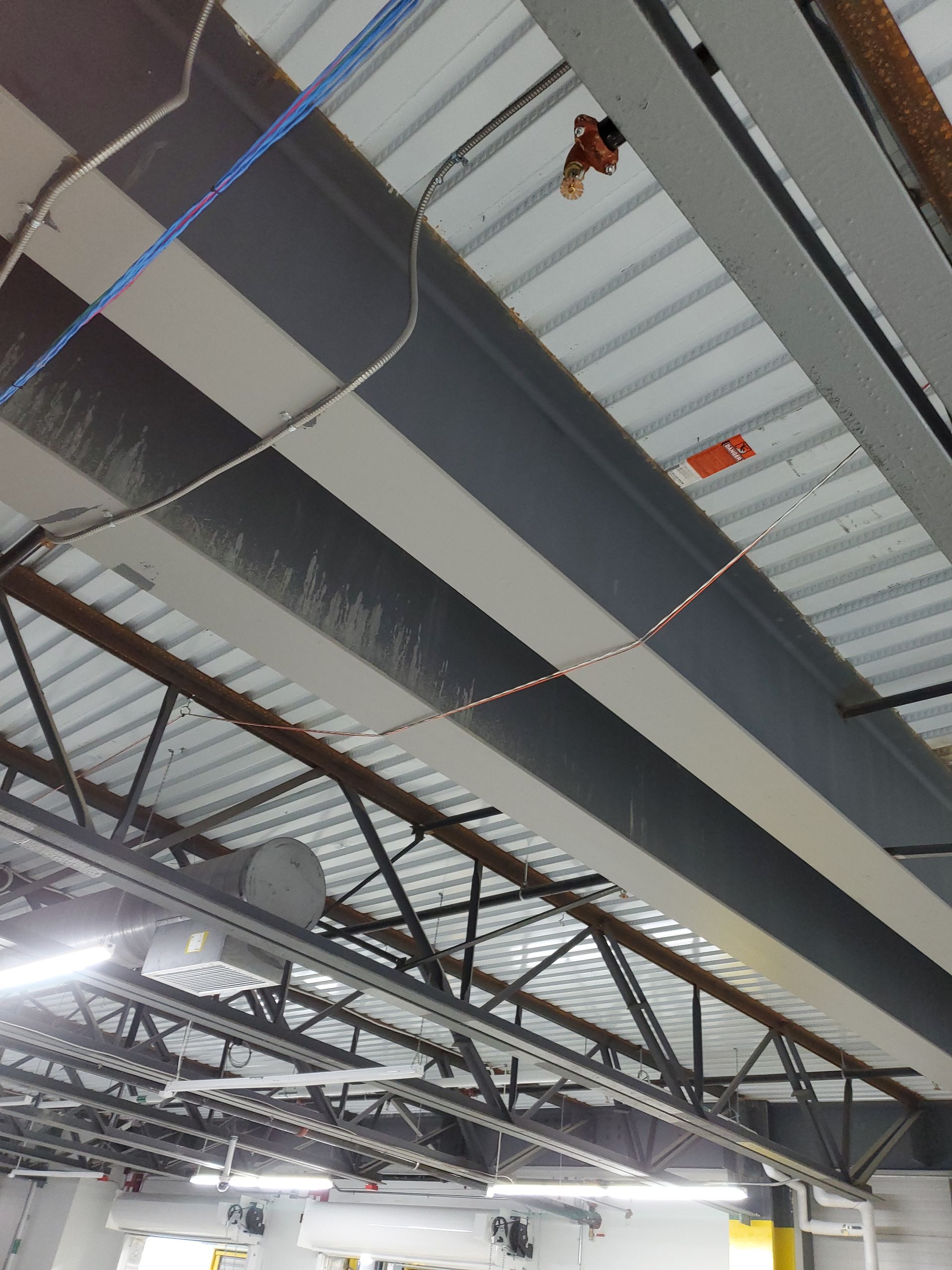 Steel beams and a corrugated metal roof, with sprinklers, wiring, and ductwork visible.