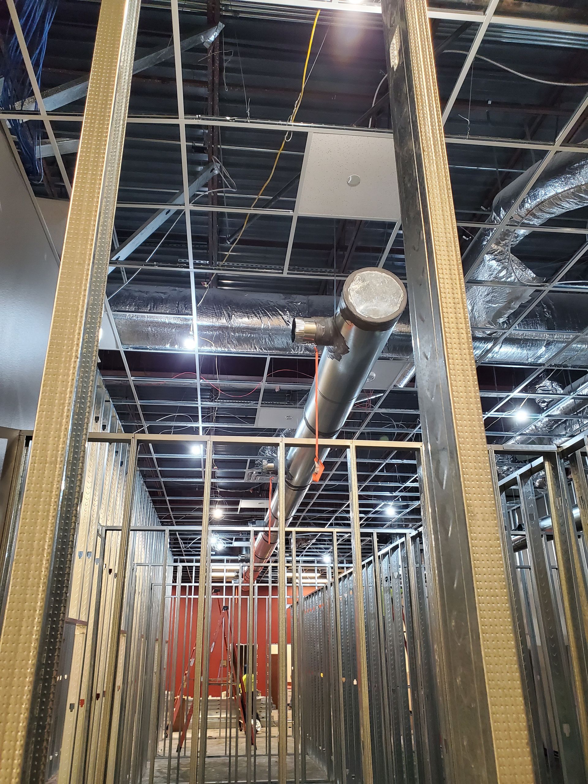 Construction site interior with metal framing and ventilation pipes.