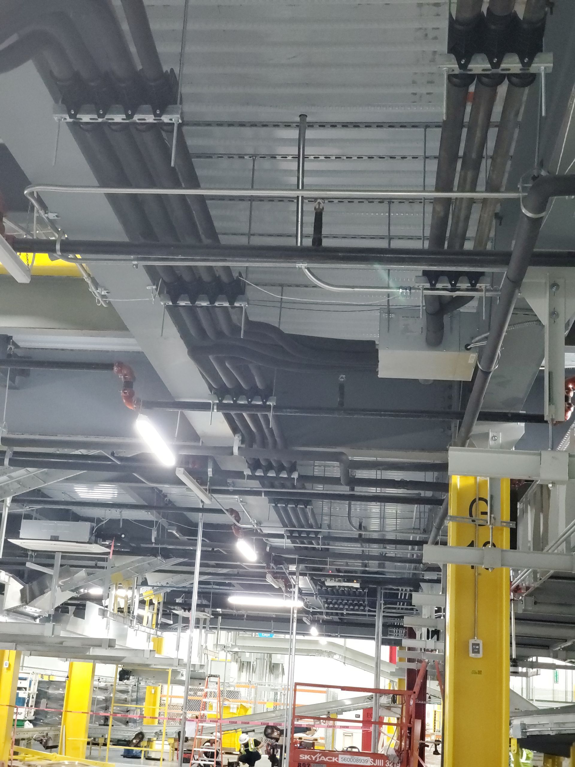 Industrial ceiling with pipes, conduits, and ventilation systems. Yellow support columns.