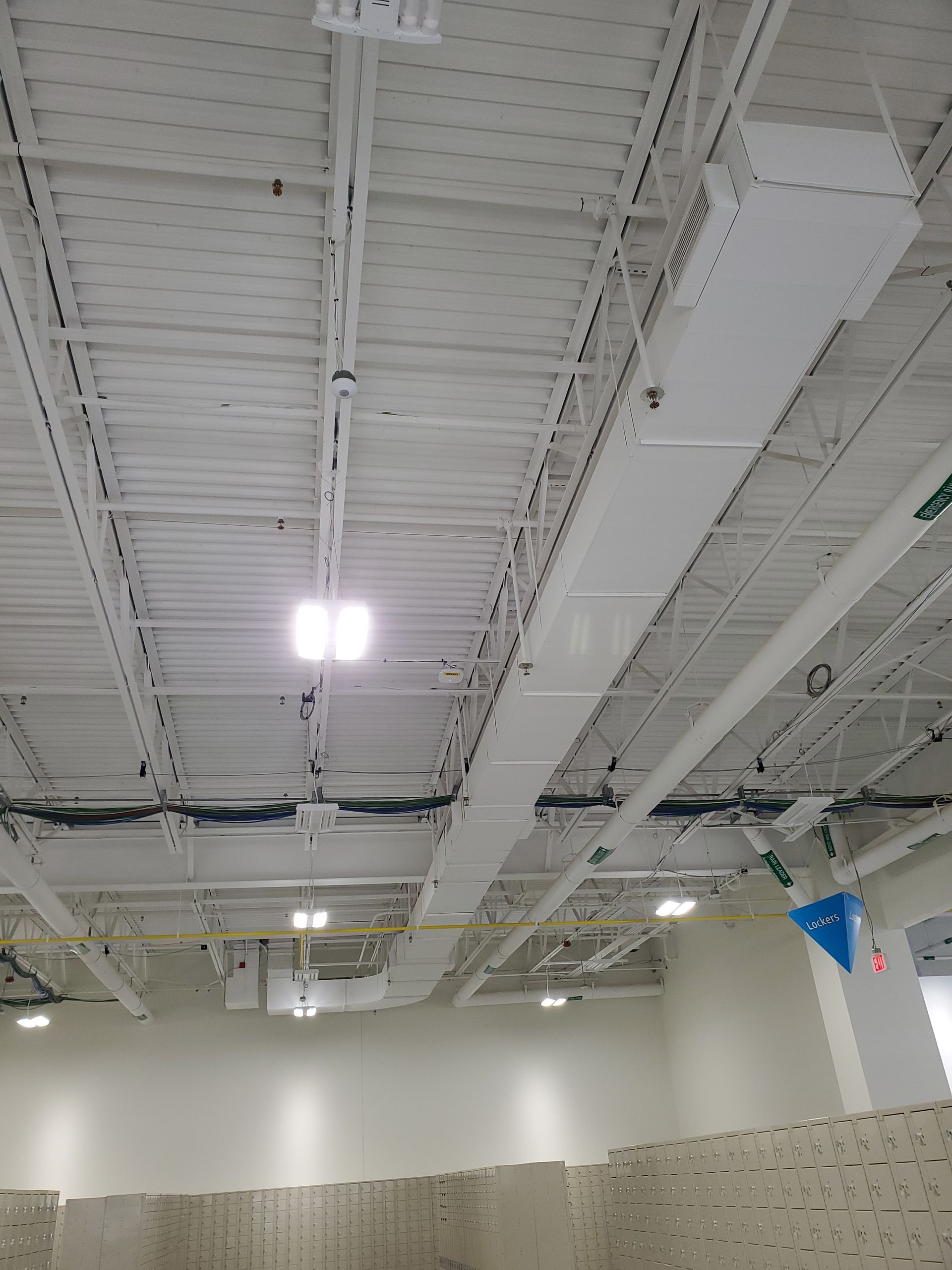 White ceiling with exposed beams, lighting, and ductwork in a large room, possibly a gymnasium.