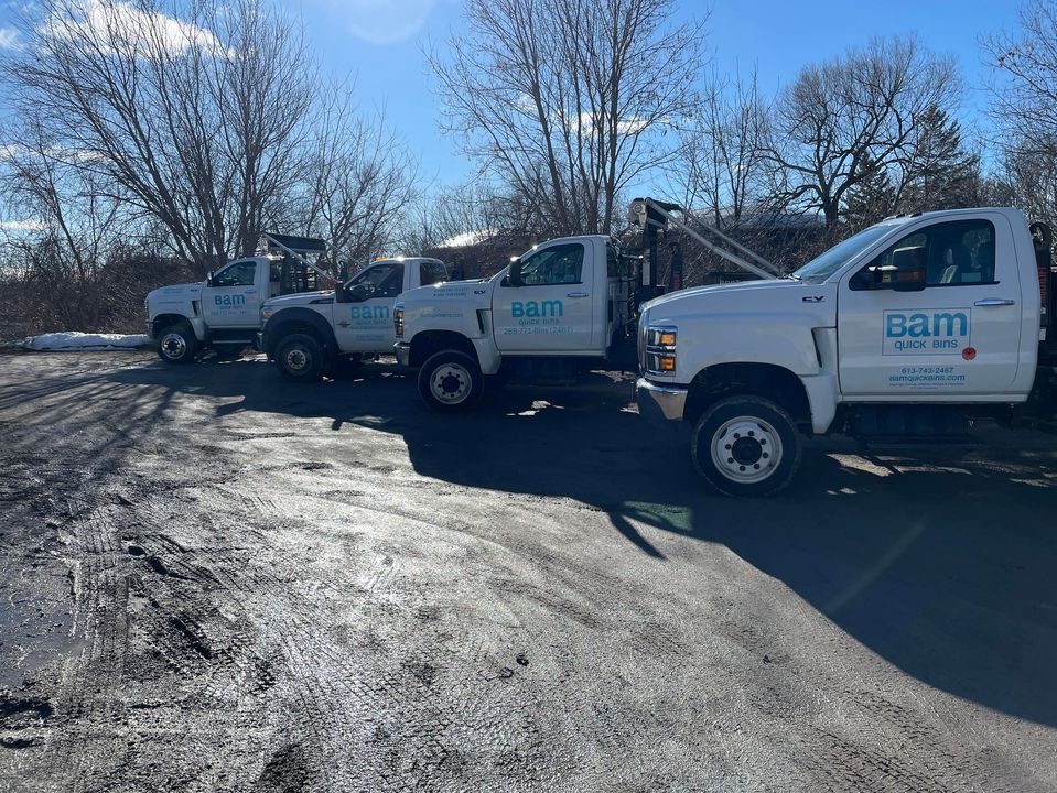 Four white tow trucks parked outside on a cloudy day.