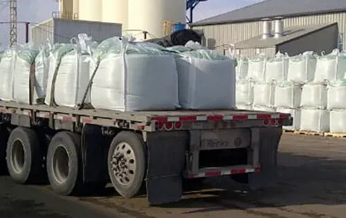 Flatbed truck carrying large white bags of material in an industrial setting.
