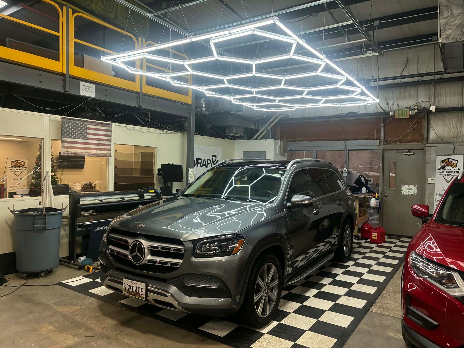 Gray Mercedes SUV parked in a car detailing bay with hexagon lights above.