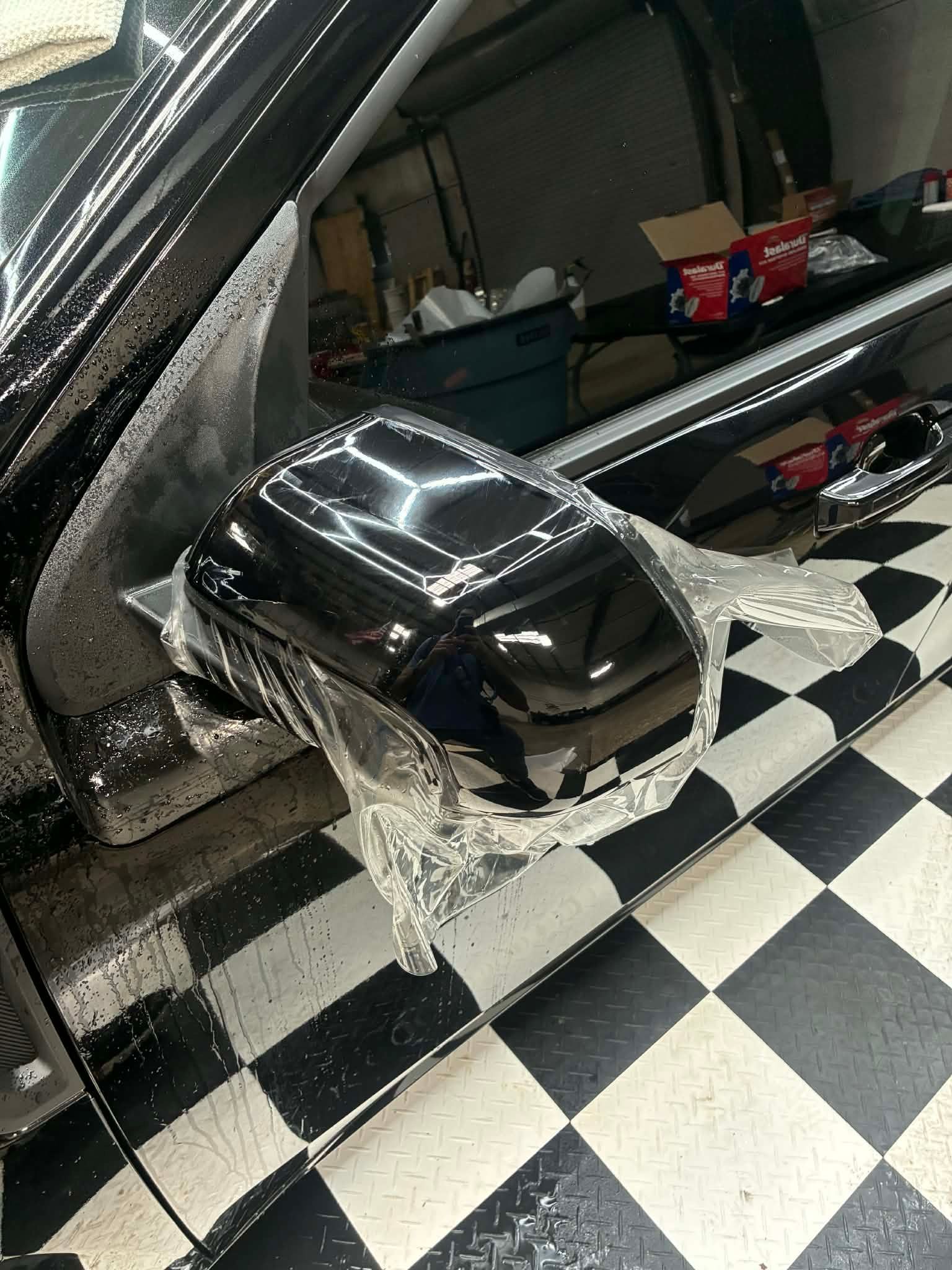 Black side mirror on a car in a garage with black-and-white checkered floor tiles