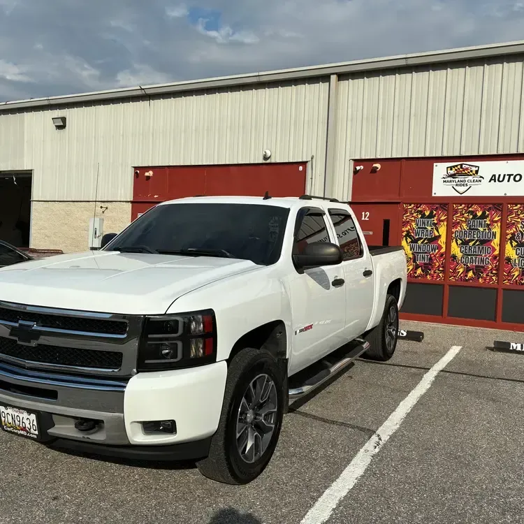 White pickup truck parked outside a storefront with red doors and colorful window display
