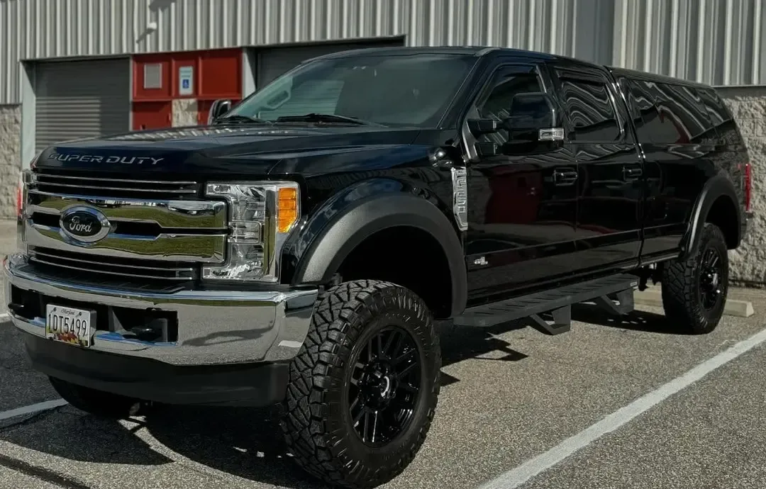Black lifted Ford Super Duty truck parked in a lot, side view