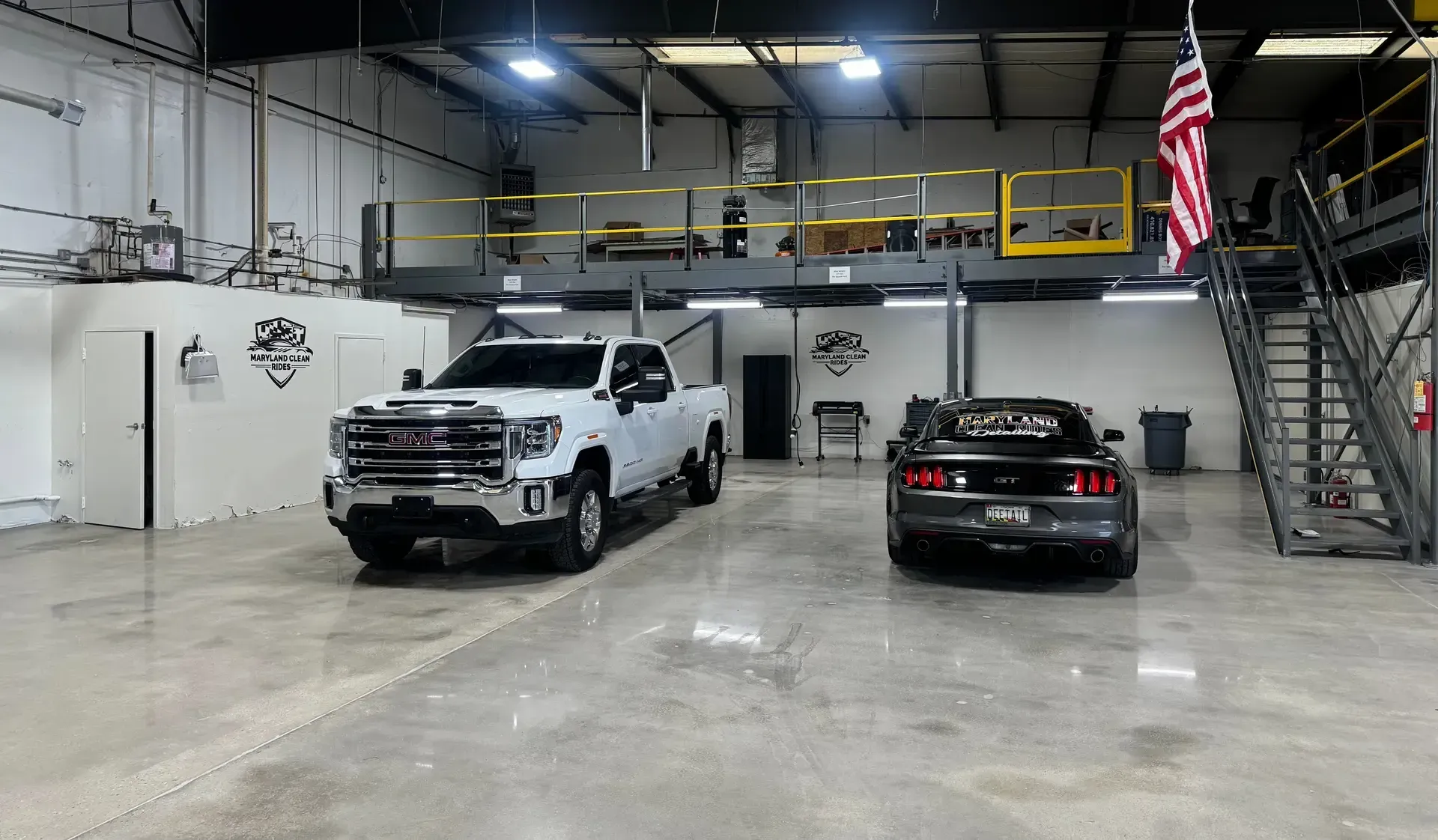 Industrial garage with a white pickup truck and black sedan parked under an American flag.