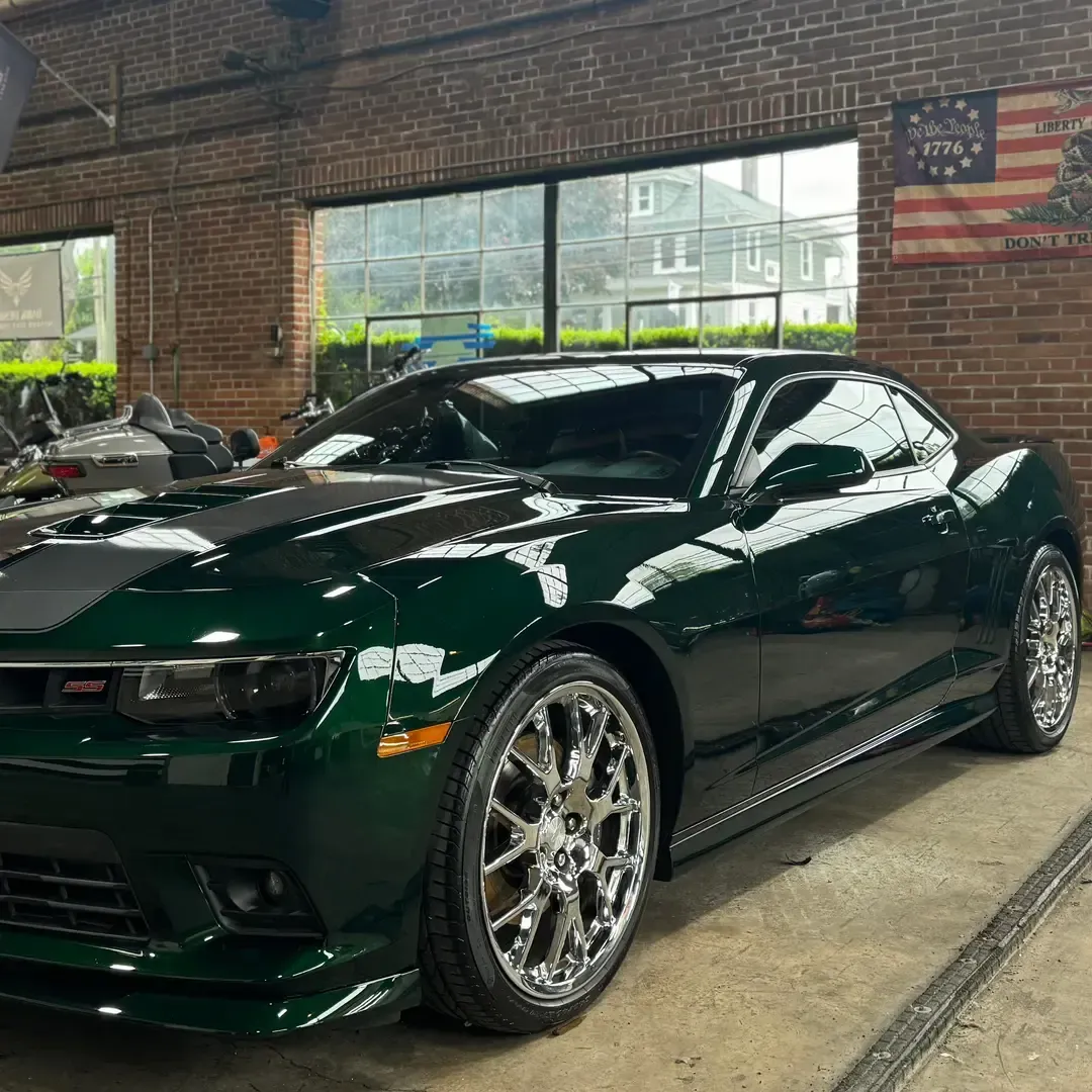 Green Chevrolet Camaro with chrome rims parked in front of a brick building.