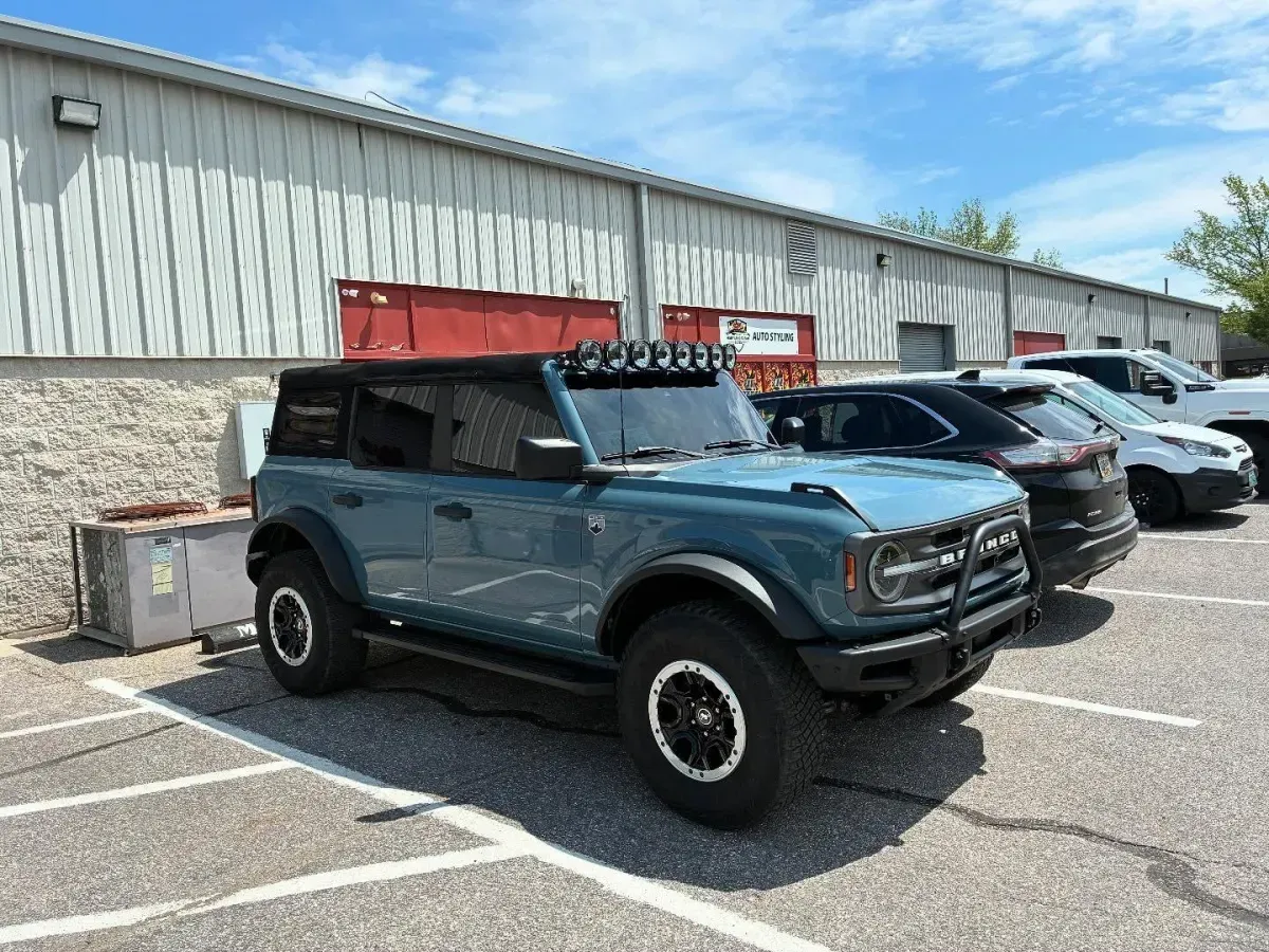 Blue off-road SUV parked beside other cars in a lot next to a warehouse building