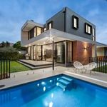 Modern two-story house with a lit backyard pool and patio seating at dusk