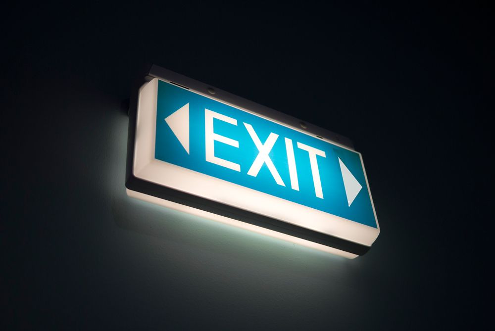 Illuminated blue EXIT sign with arrows on a dark wall.