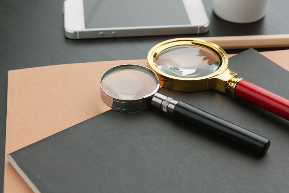 Two magnifying glasses on black and tan notebooks; phone and pencil in the background.