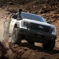 White Ford pickup navigating a rocky off-road trail, front three-quarter view with dust and rugged terrain.