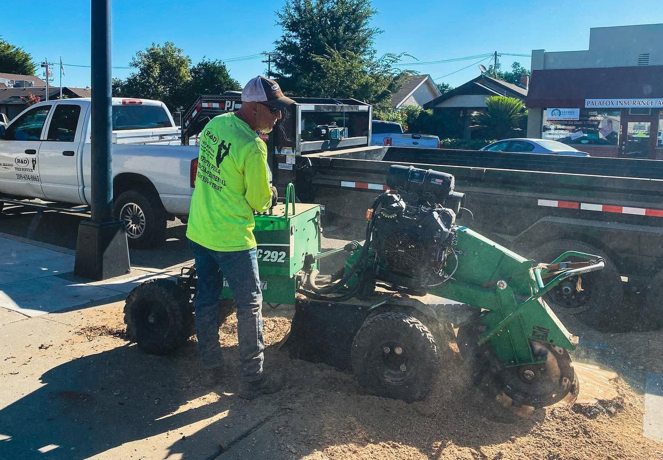 Worker in neon safety gear operating a green mower on a dusty roadside with cars and tents nearby