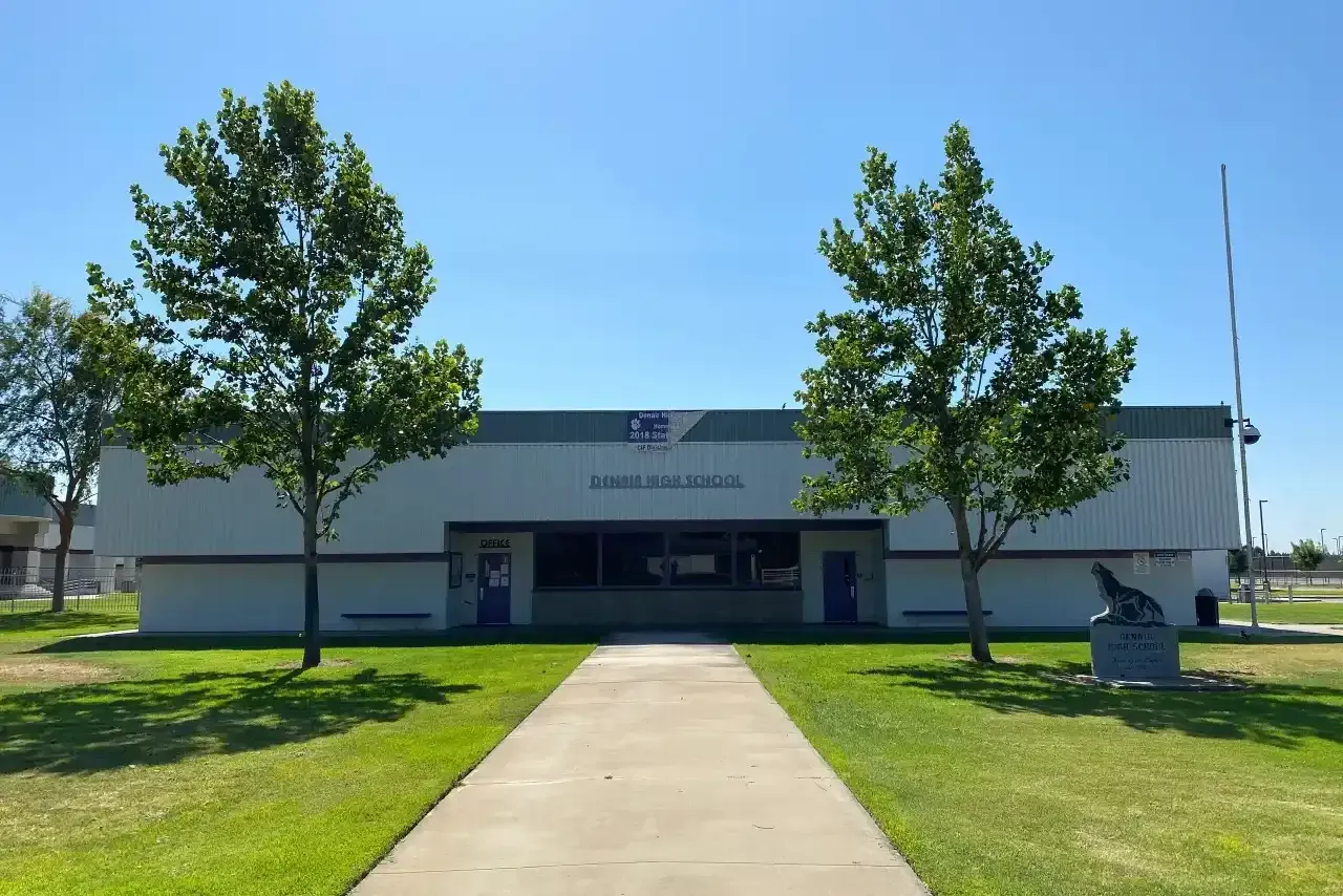 Front view of a white building with a central entrance, flanked by two trees and a walkway.